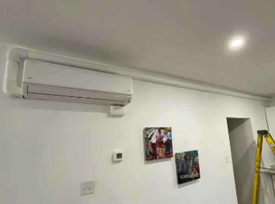 A finished mini-split installation, the white cover carrying the pipework in a straight line up the wall to the ceiling